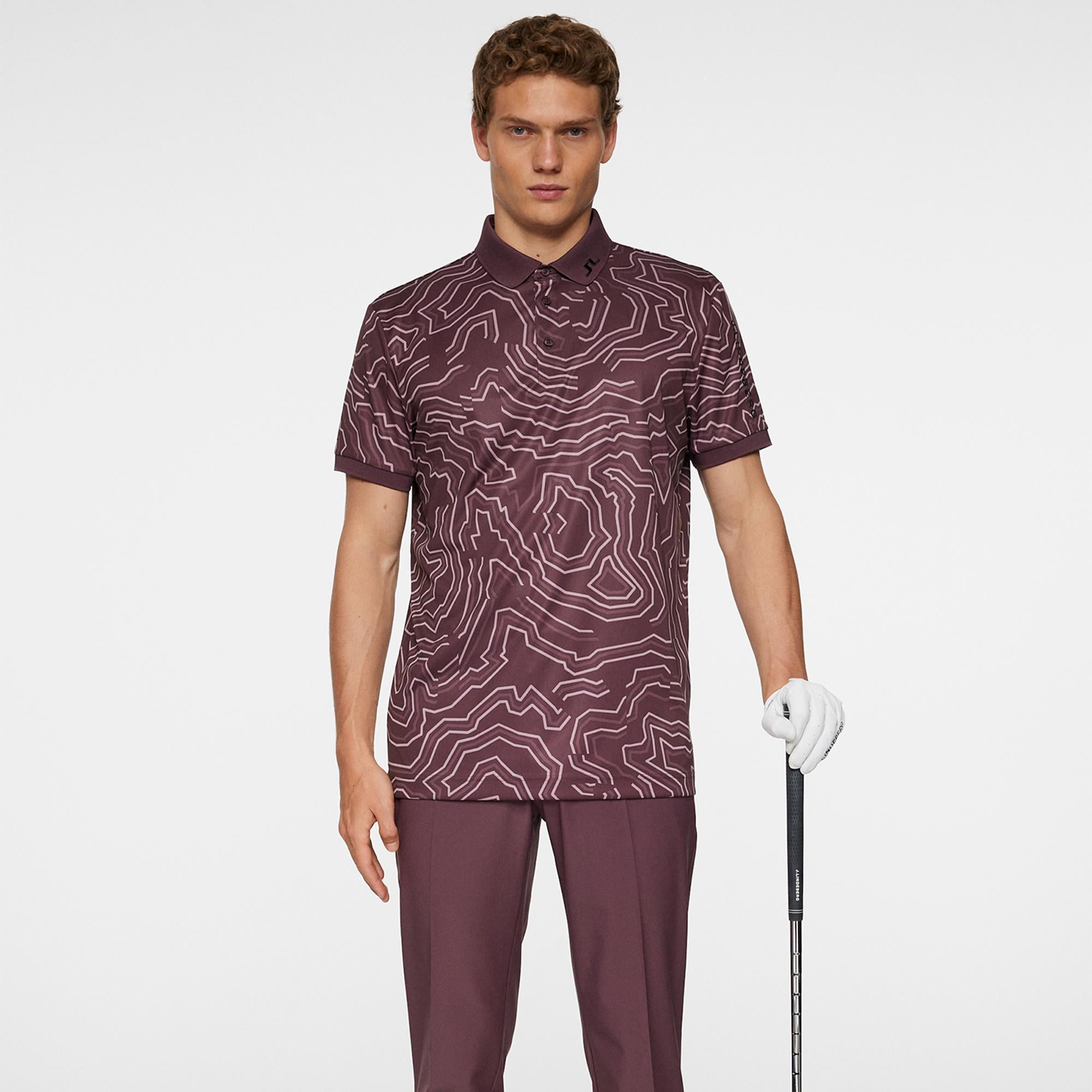 Model wearing J.Lindeberg men’s golf polo shirt holding golf club in Topo Huckleberry – Teepeg golf collection